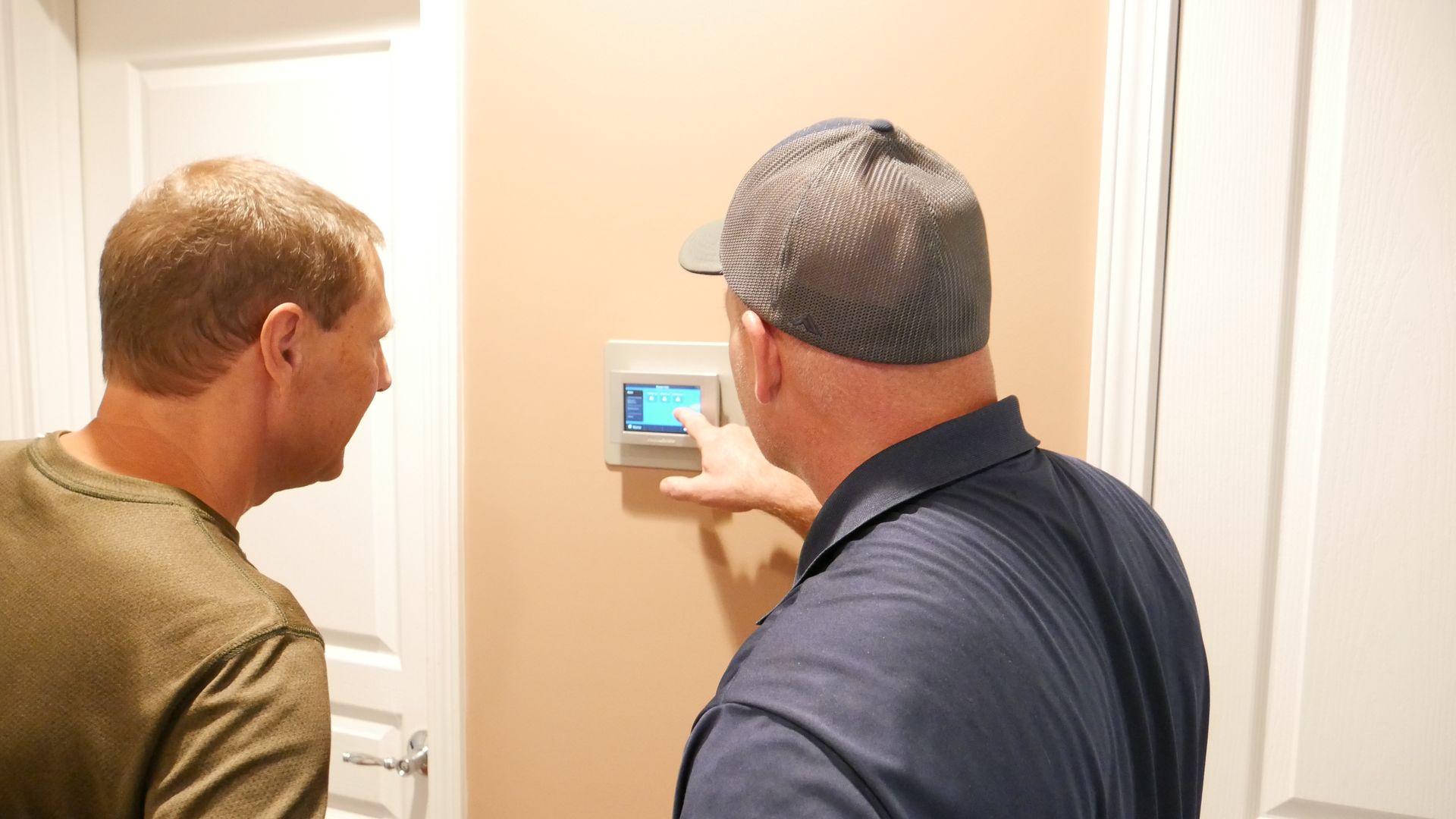 two men are looking at a thermostat on a wall .