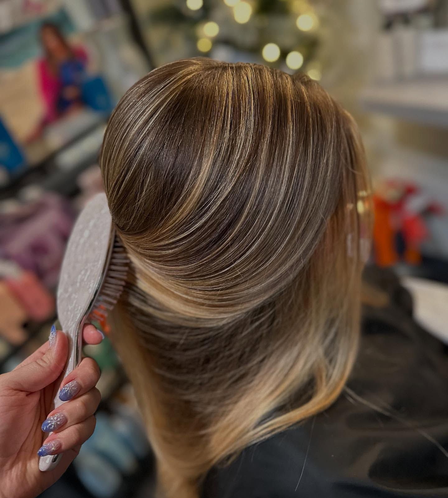 Hand brushing shiny brown-blonde hair in a salon setting