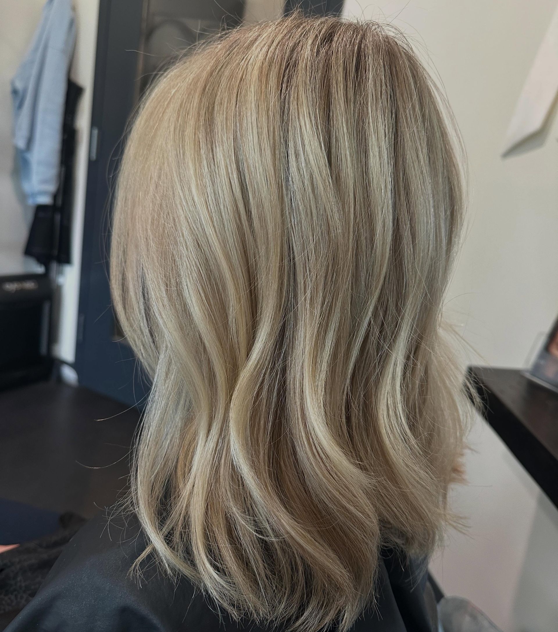 Blonde layered haircut with soft waves, shown from the back in a salon setting