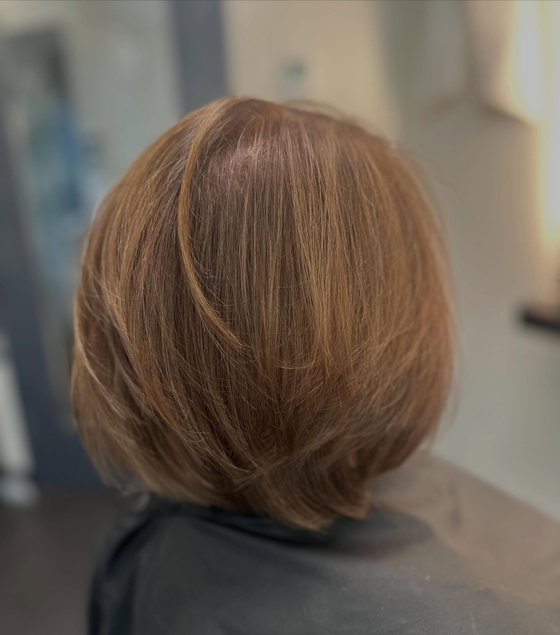 Short layered brown haircut with subtle highlights, viewed from the back in a salon.