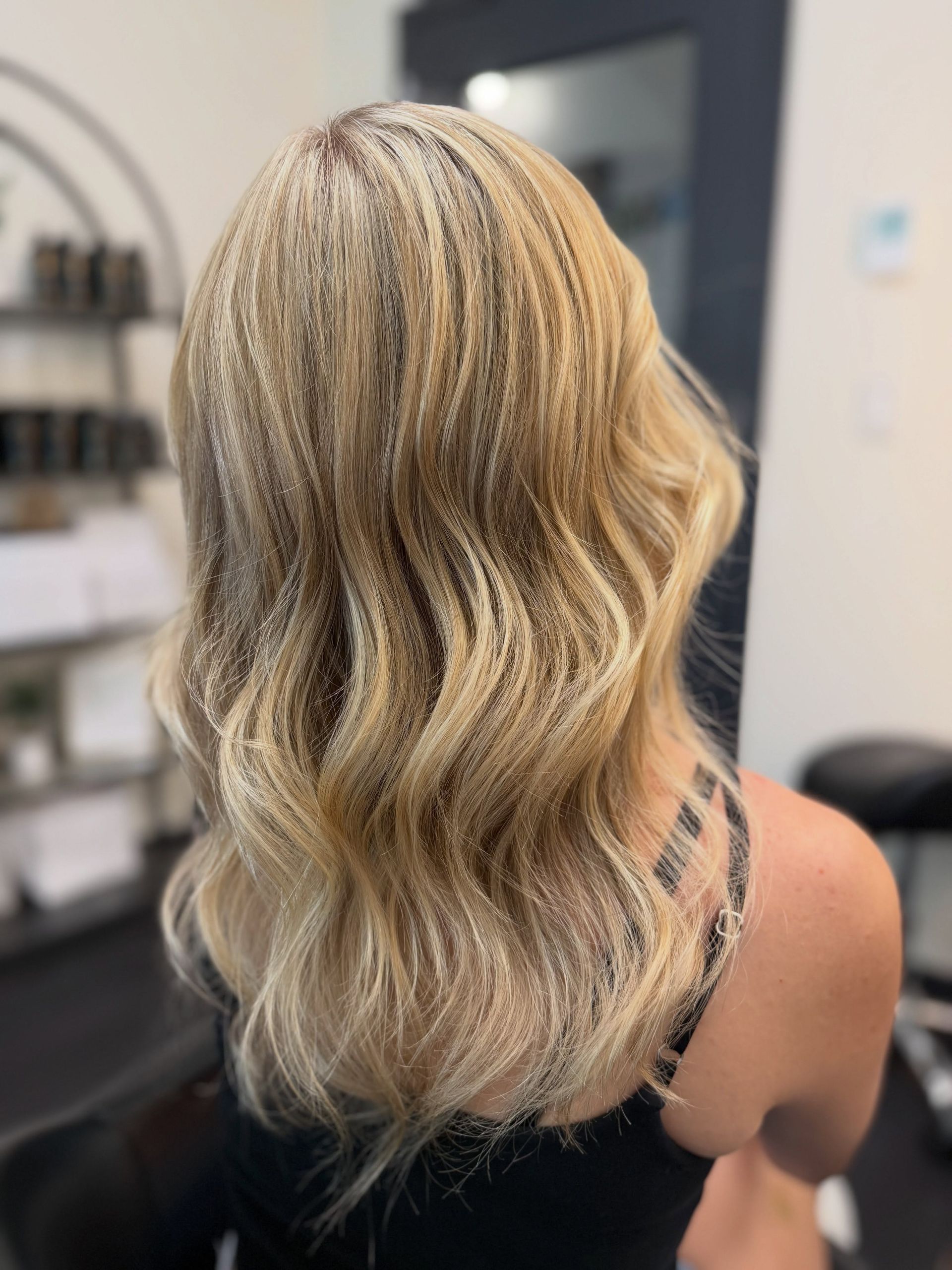Blonde wavy shoulder-length hair with dark roots and soft highlights in a salon setting