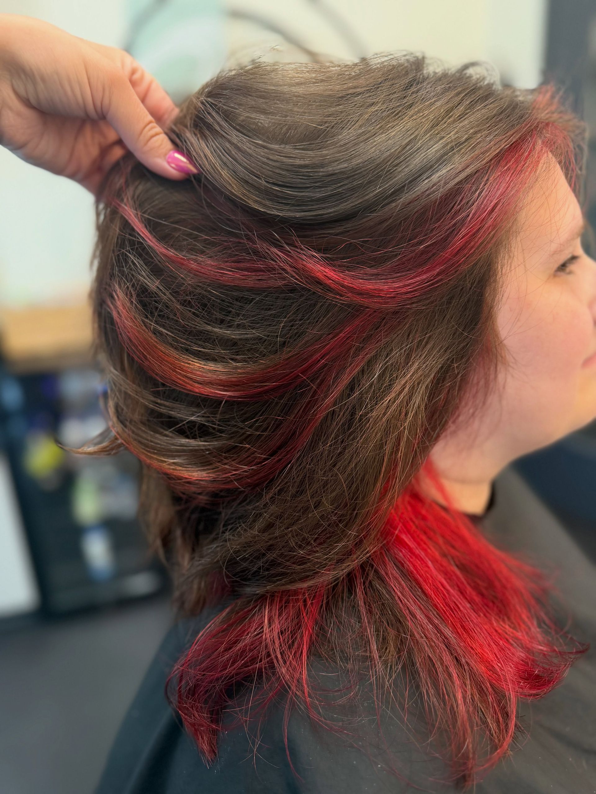 Side view of layered dark hair with bright red highlights being held up at a salon.