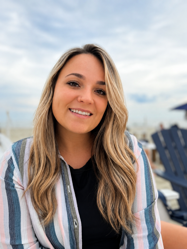 Smiling woman outdoors on a beach chair with ocean and cloudy sky in the background