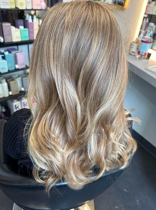 Wavy blonde balayage hairstyle seen from behind in a salon chair