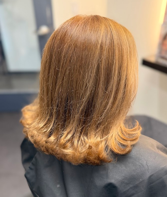 Back view of a shoulder-length layered haircut with warm brown and caramel highlights in a salon chair