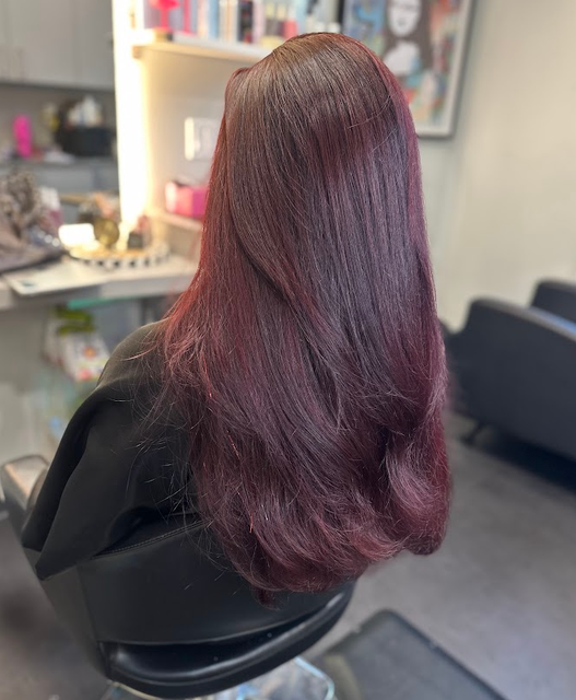 Back view of long burgundy hair in a salon chair, with soft waves at the ends