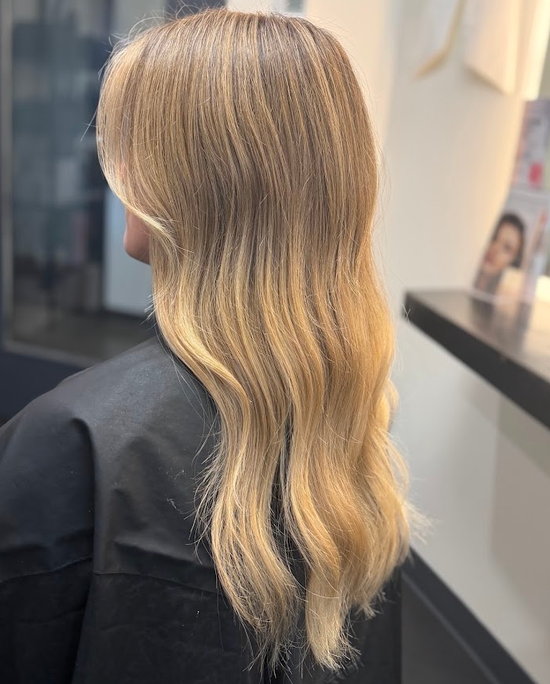 Blonde wavy shoulder-length haircut with darker roots in a salon setting