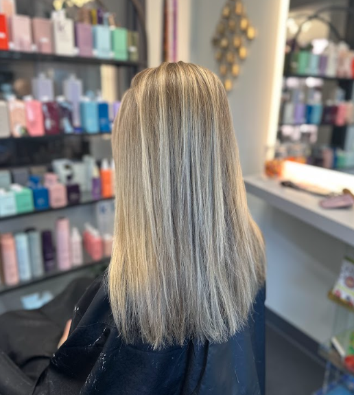 Blonde hair seen from behind in a salon, with product shelves in the background