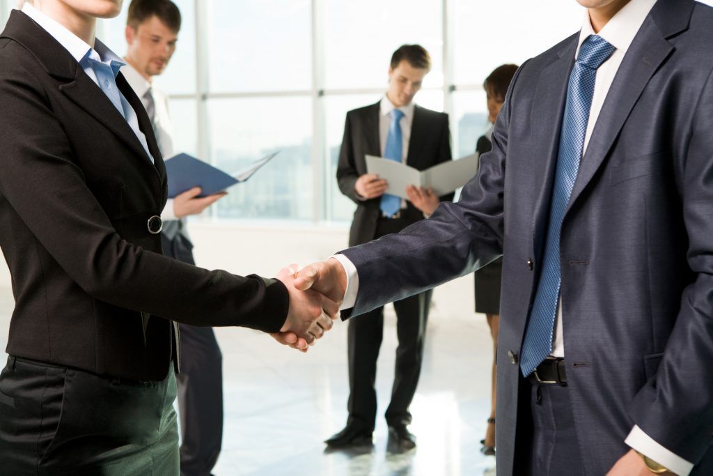 Businesspeople shaking hands; colleagues in the background.