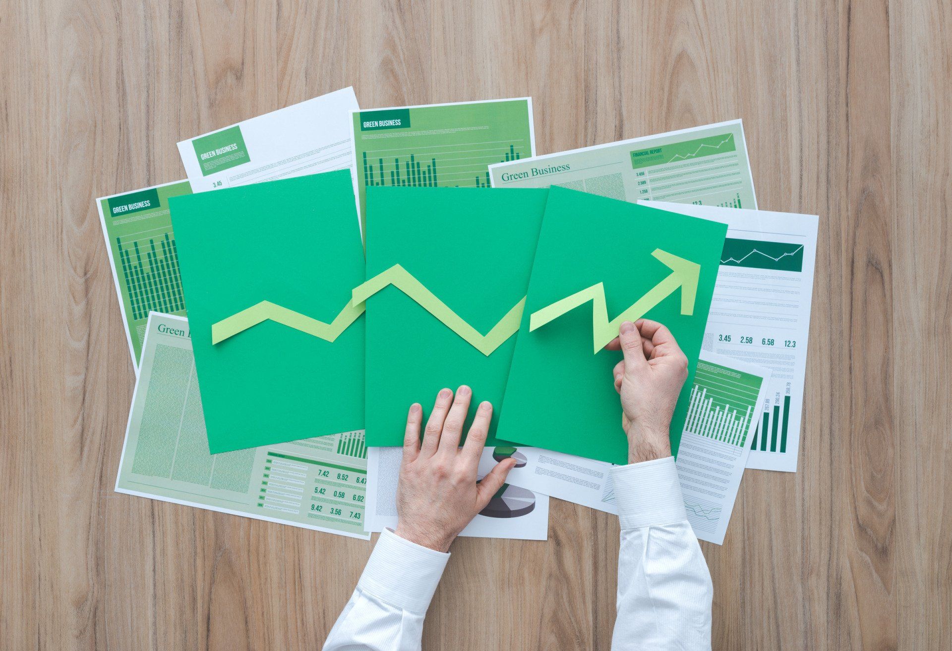 Hands arranging a green paper arrow over financial documents, symbolizing growth and positive trends.