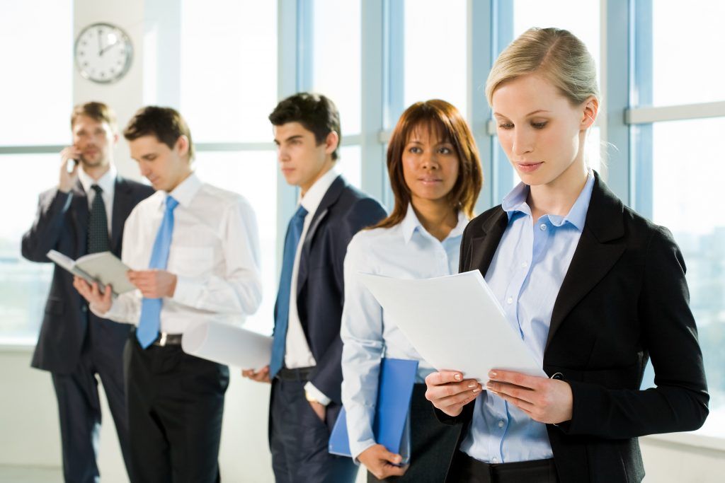 Business professionals reviewing documents, standing in a brightly lit office.