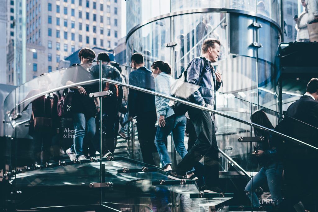 People walking up stairs with a railing. Tall buildings in the background.