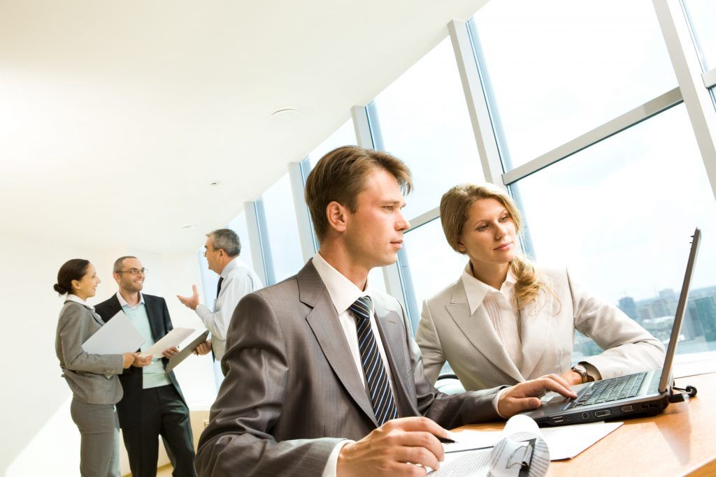 Businesspeople working in an office with a laptop, documents, and large windows.