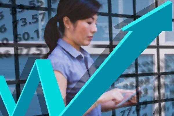 Woman using a tablet with a blue upward trending arrow overlaid on a stock market data background.