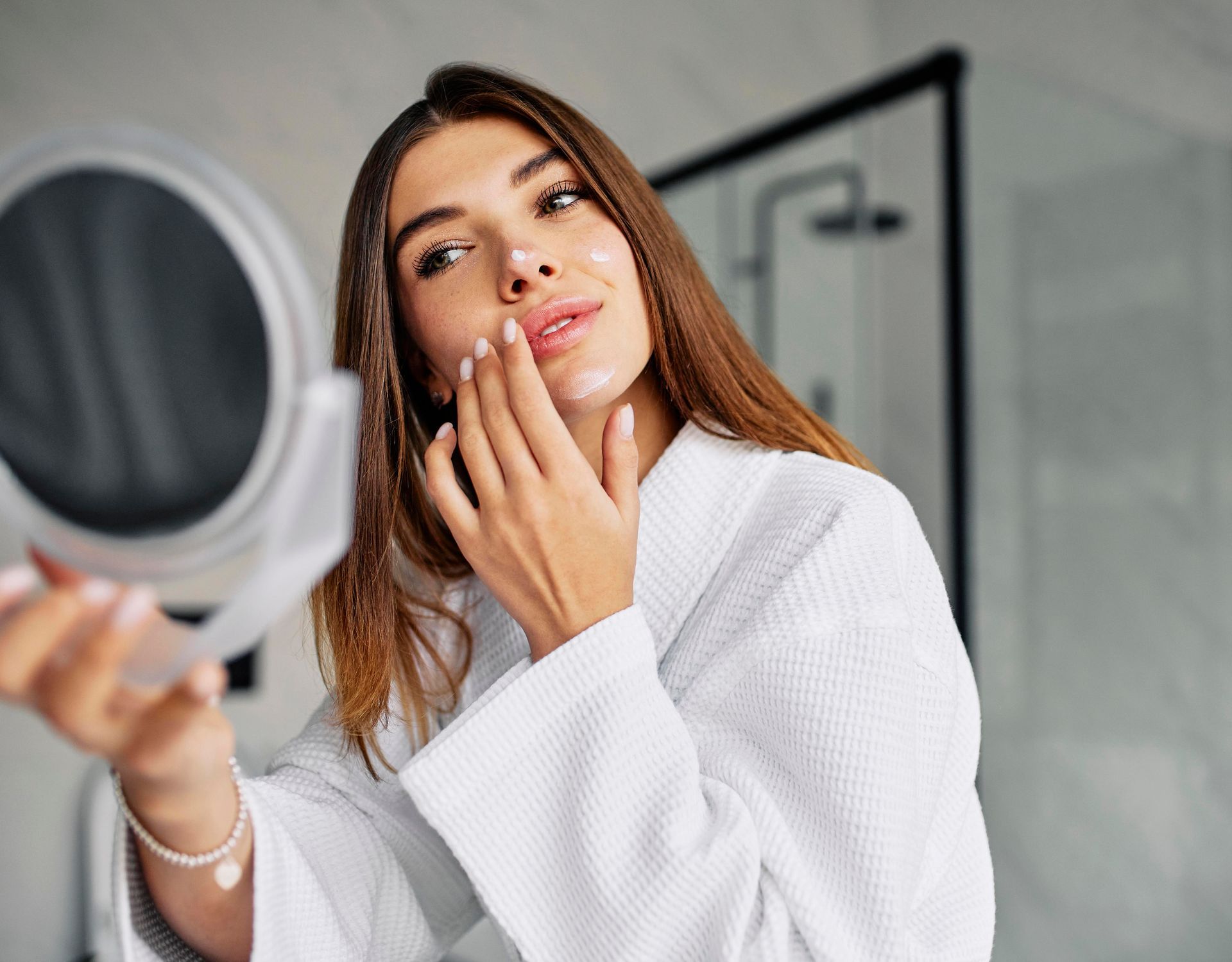 A woman is looking at her face in a mirror.