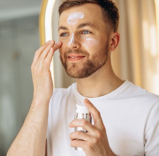 A man with a beard is applying lotion to his face.