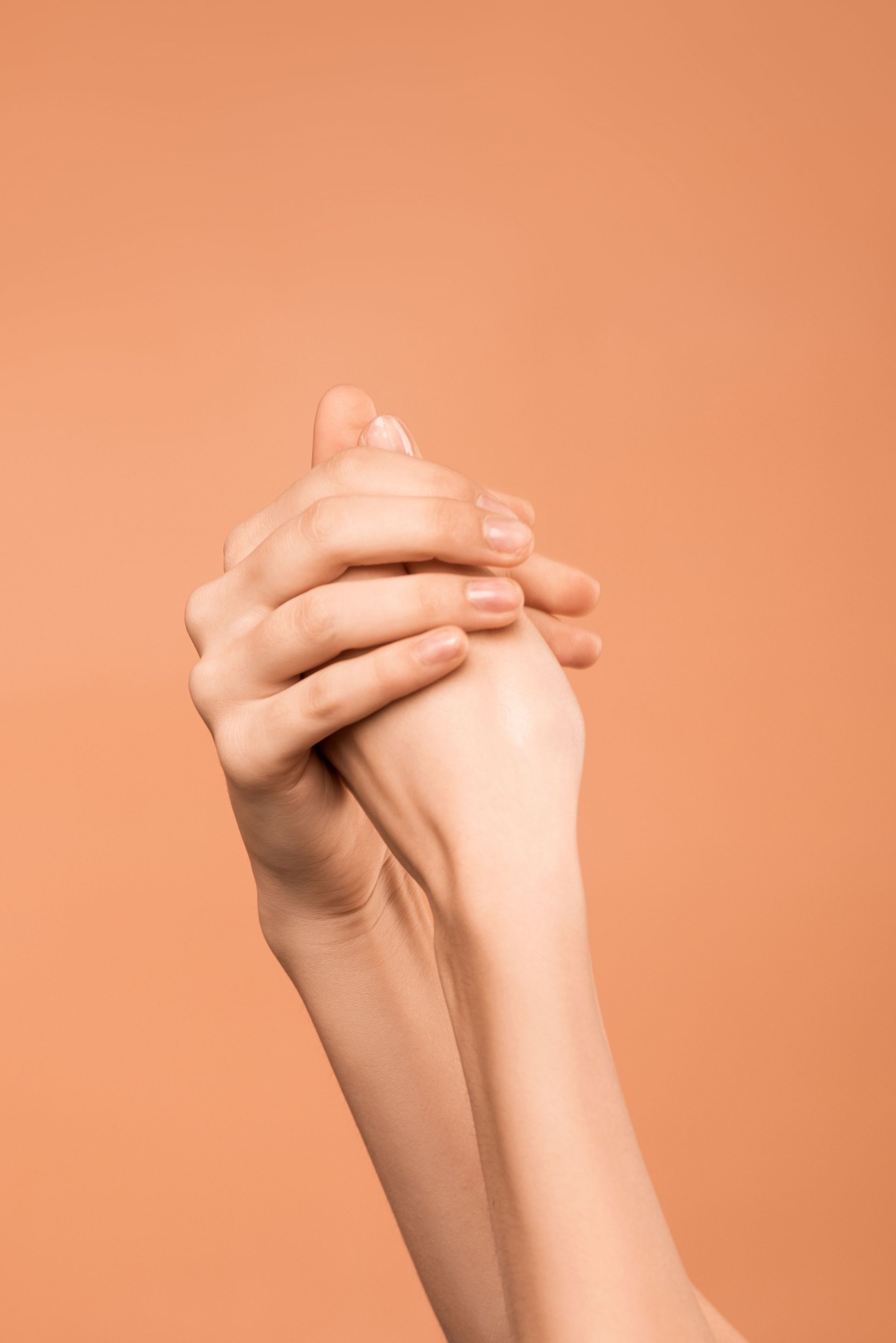 Two clasped hands against a soft orange background
