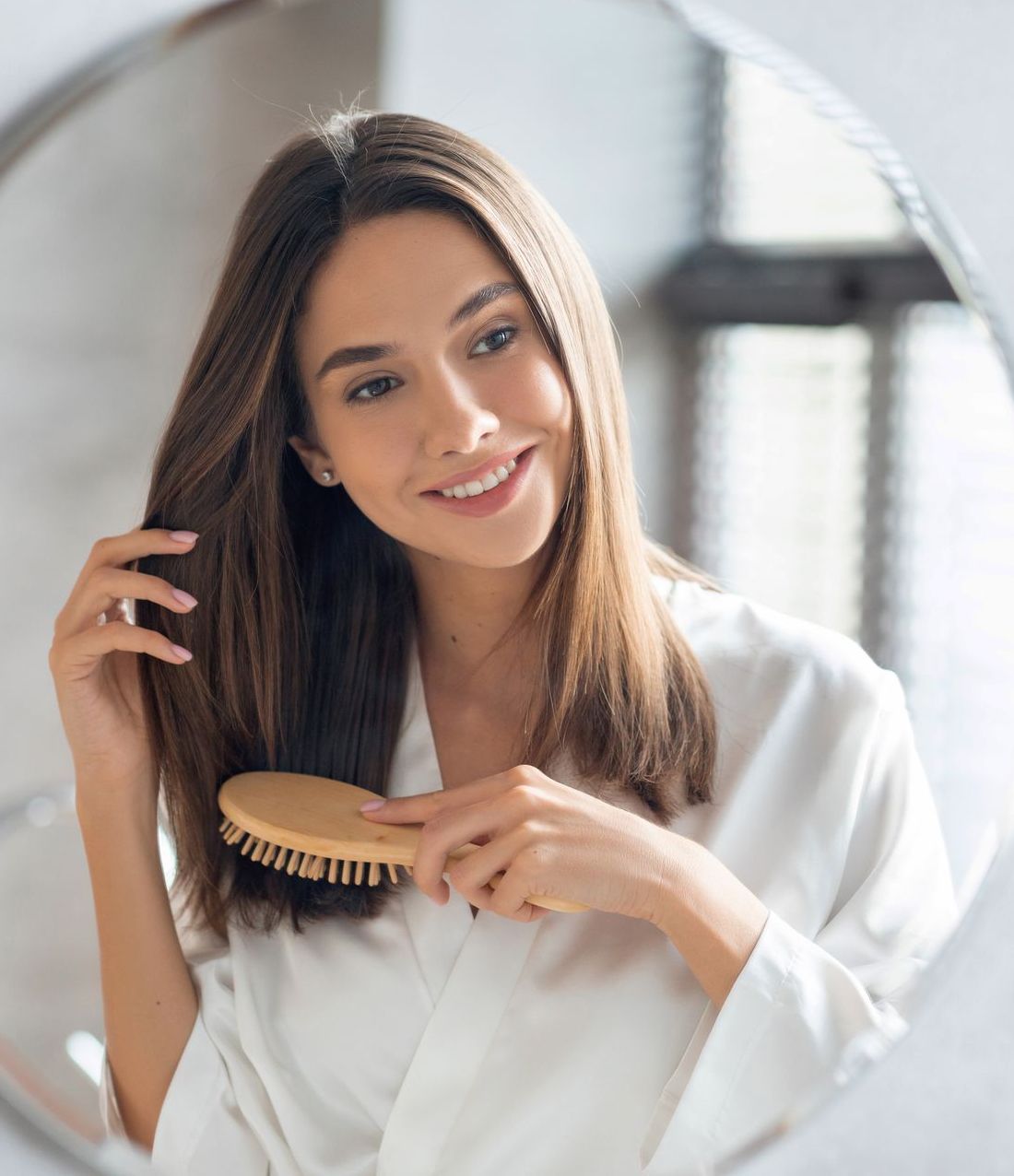 A woman is brushing her hair in front of a mirror.