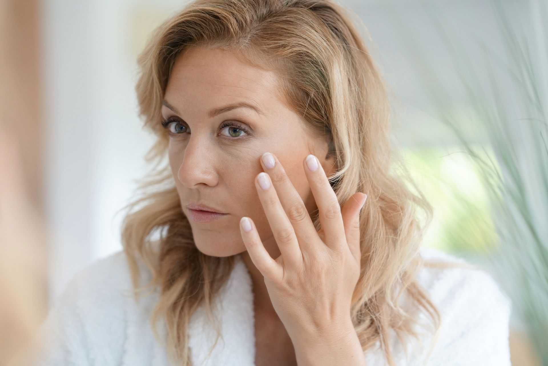 A woman is looking at her face in the mirror.