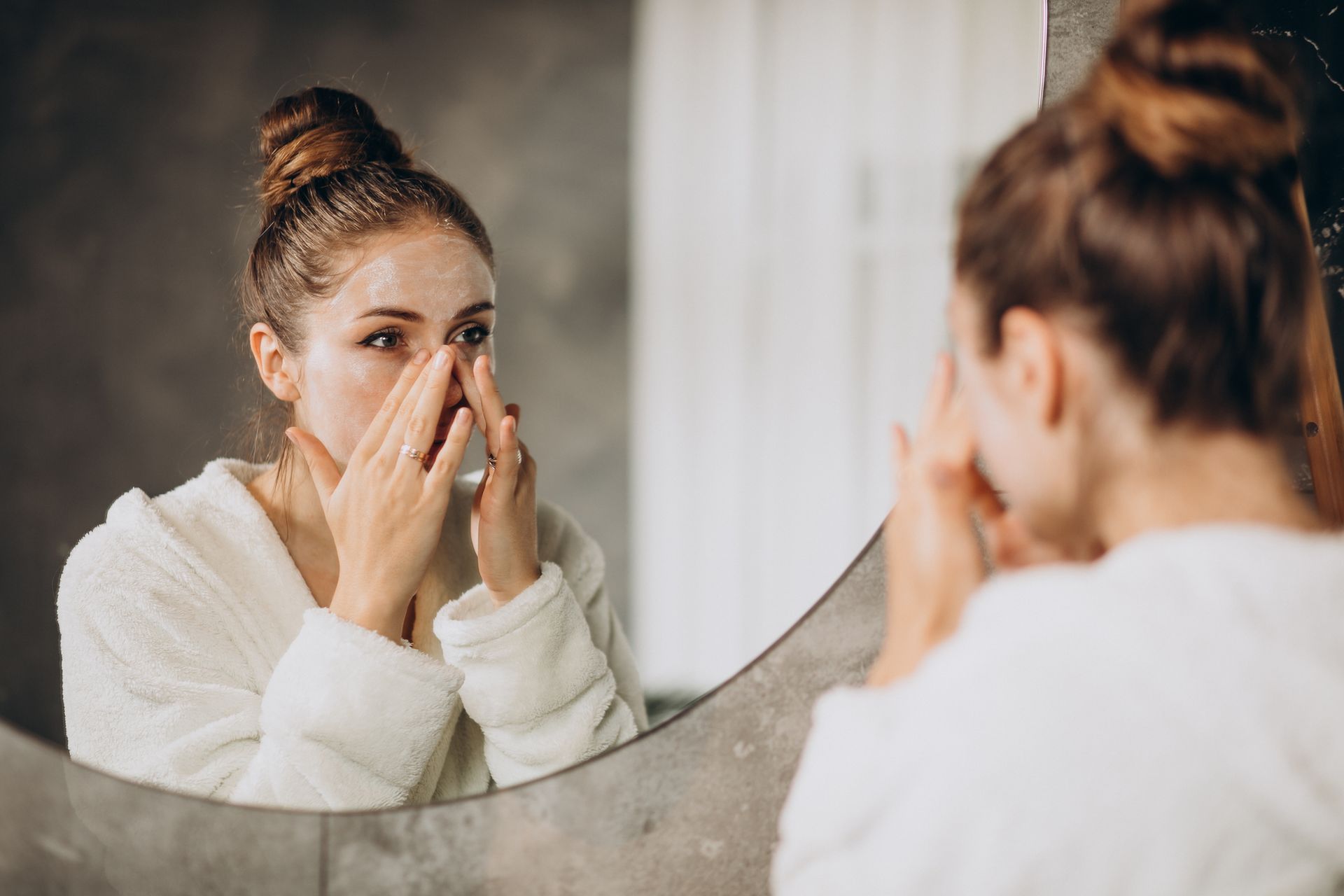 A woman is looking at her face in the mirror.