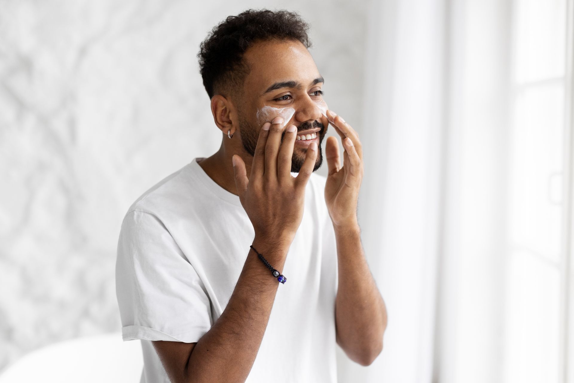 A man is applying cream to his face in front of a mirror.