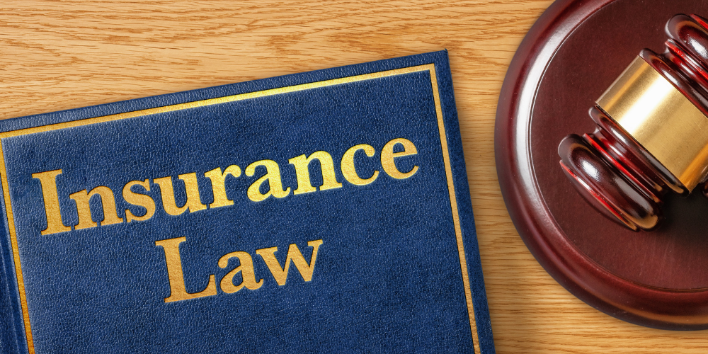 Blue “Insurance Law” book beside a judge’s gavel on a wooden surface