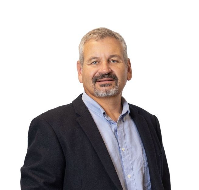 Chris Coetzee - DormFIN in a blazer and open-collared blue shirt smiles against a white backdrop.