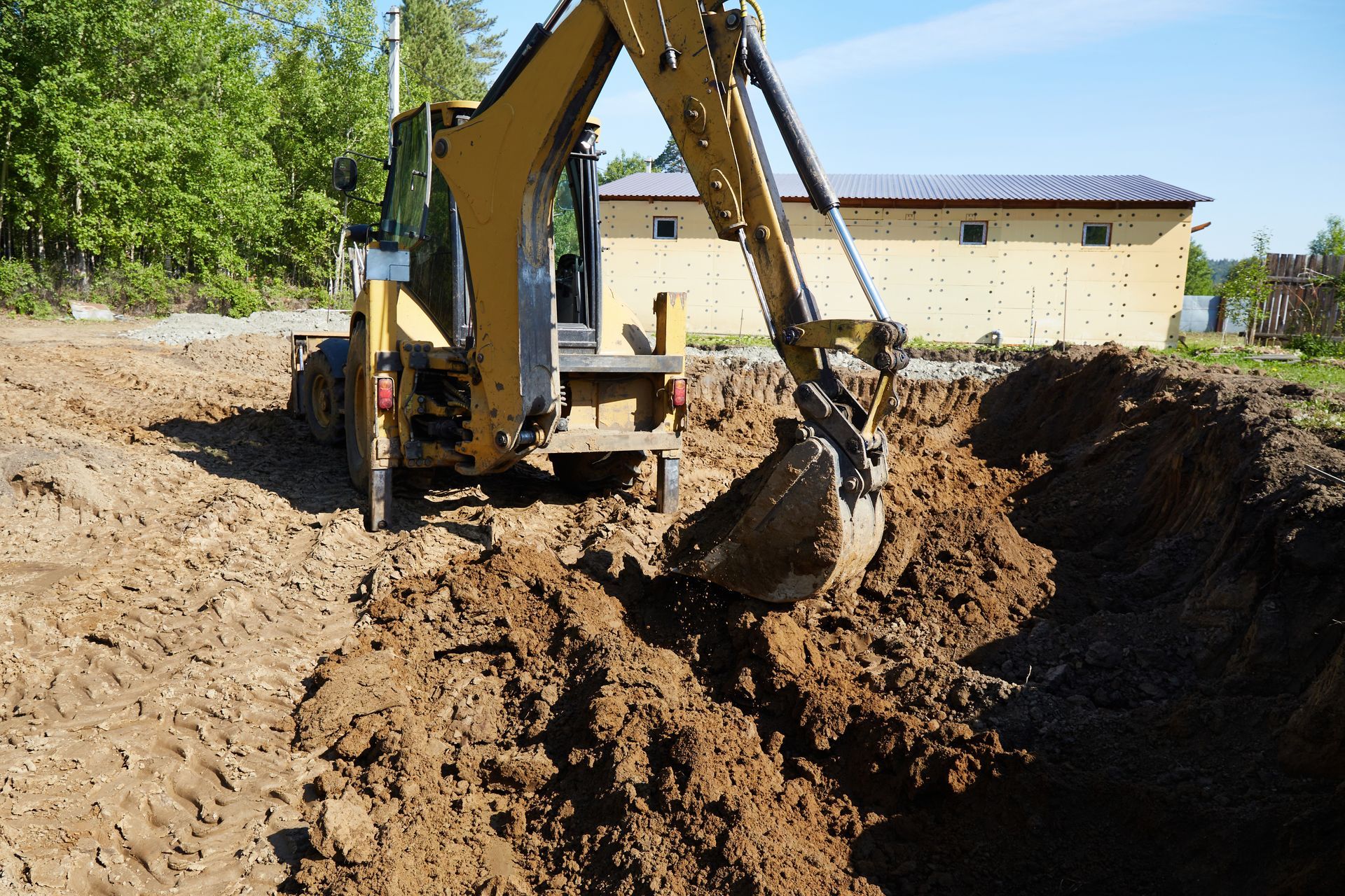 Workers and a skid steer on a dirt field near a green hillside at sunset