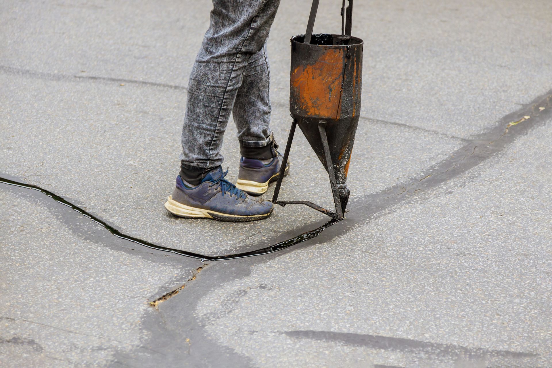 Worker sealing asphalt on a residential street in autumn.