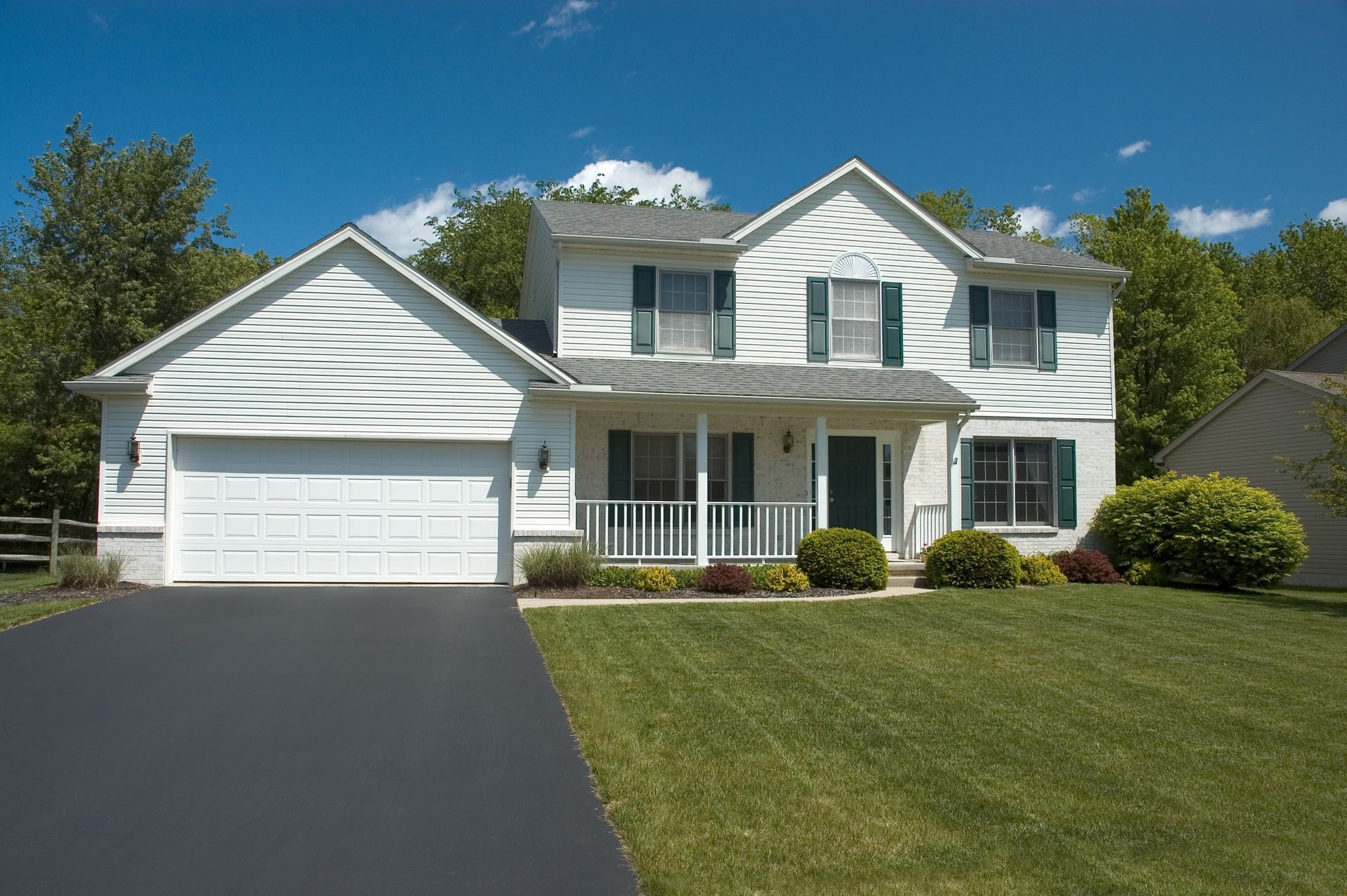 Suburban two-story white house with a two-car garage, front porch, and a green lawn under a blue sky