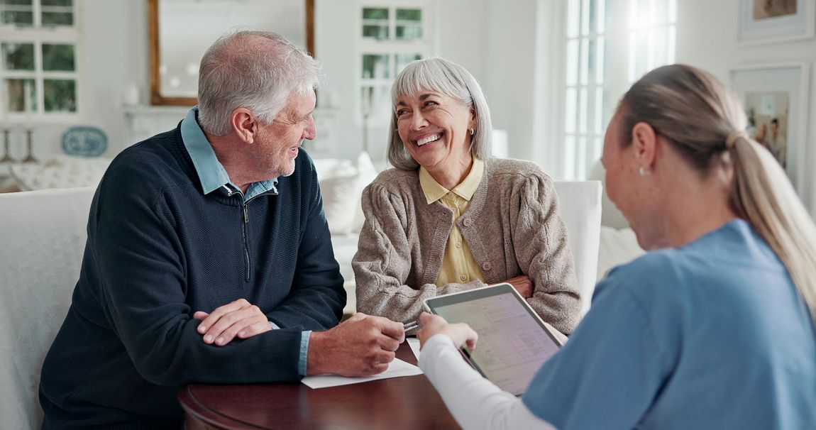 Three people meeting at a table, discussing paperwork in a bright living room.