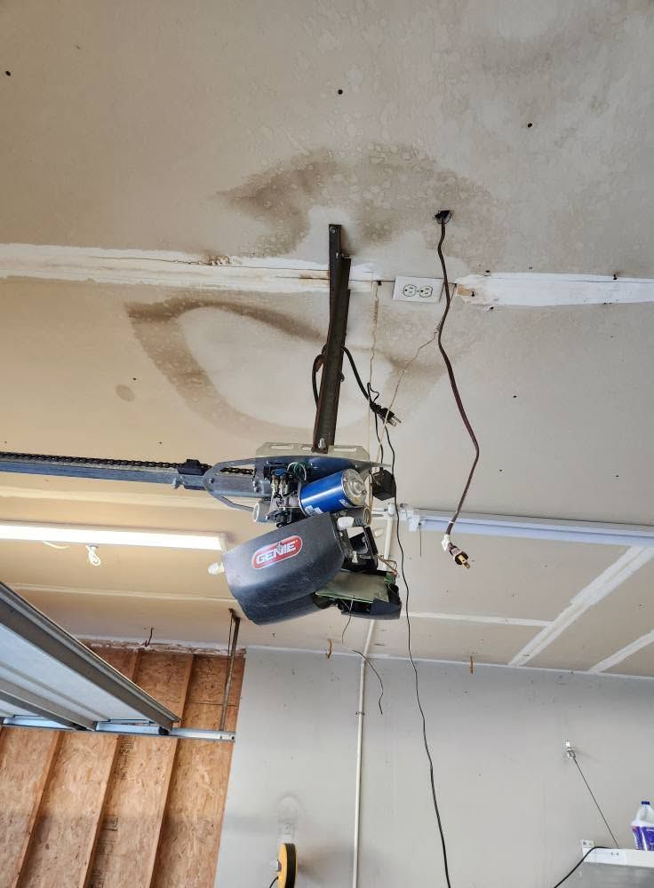 Garage ceiling with a blue and black garage door opener hanging from exposed wiring and tracks
