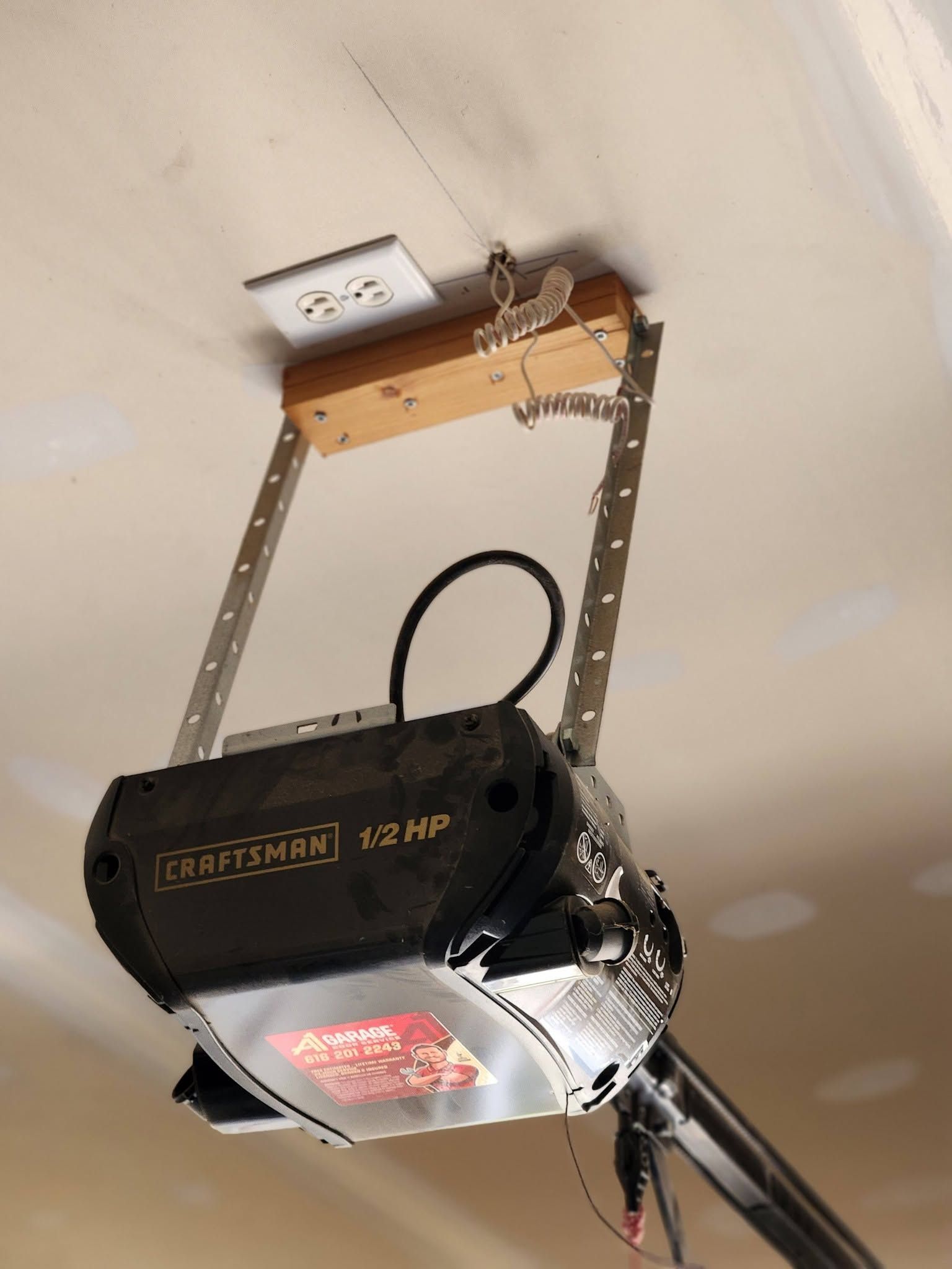 Black garage door opener mounted to ceiling with metal brackets and wiring