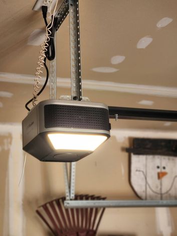 Garage door opener mounted on the ceiling, with a lit lamp and exposed metal track.