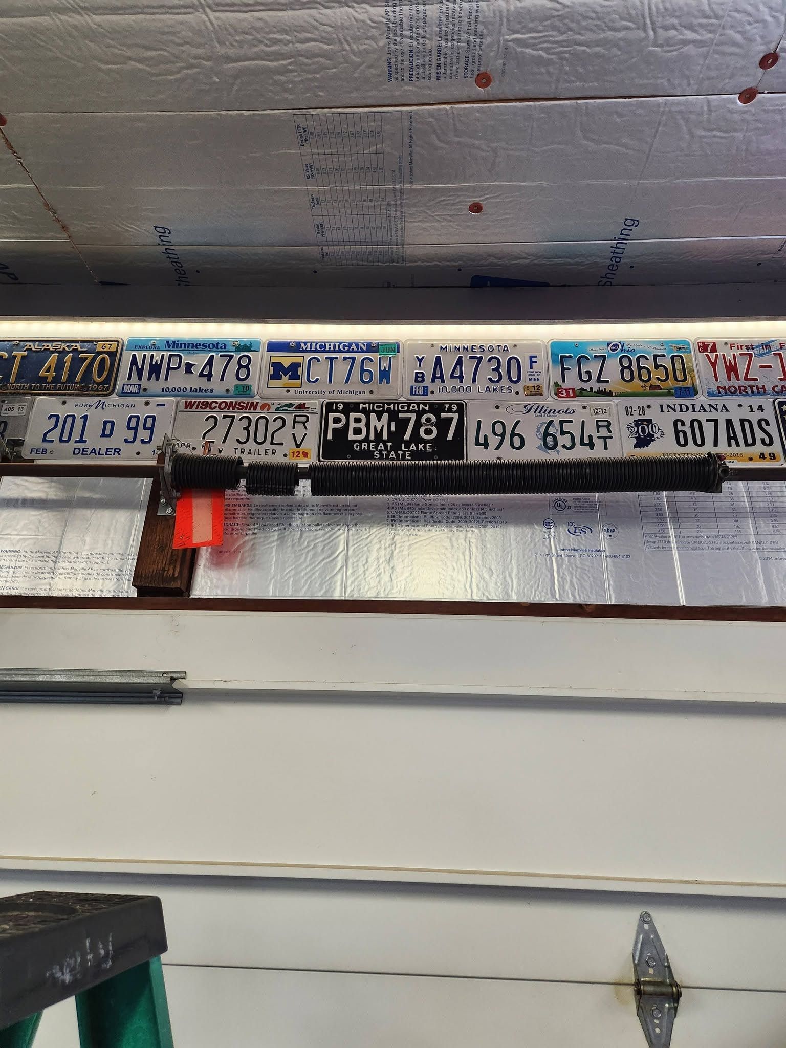 License plates mounted on a wall above a garage door, with a red hanging light.