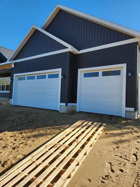 New house exterior with two white garage doors and blue-gray siding under construction
