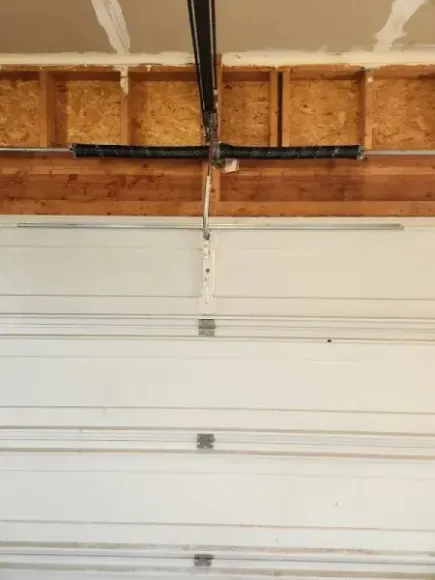 White garage door under exposed wooden rafters with black ceiling tracks above