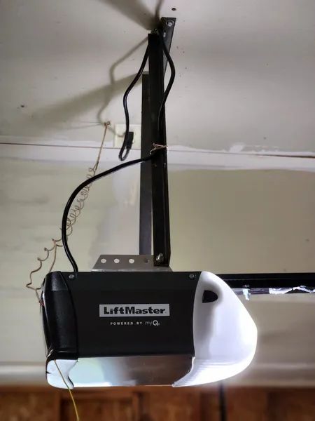 Ceiling-mounted black LiftMaster garage door opener with white light cover and hanging wires