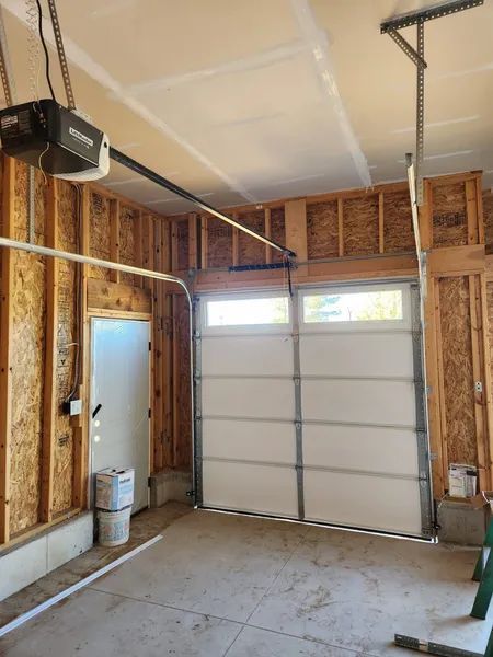 Empty residential garage interior with white sectional door, exposed wood framing, and concrete floor