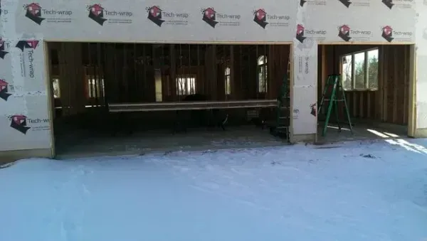 Partially built house exterior with snow-covered ground and open garage bays