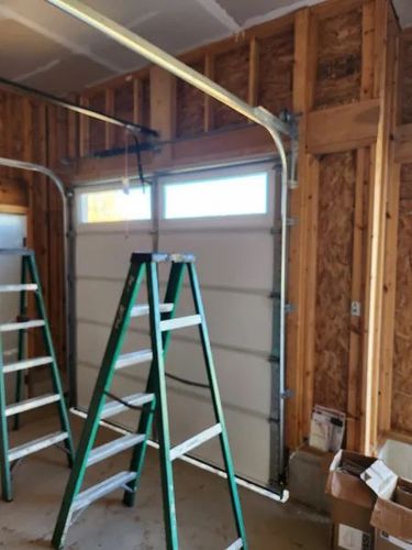 Two ladders in an unfinished garage beside a closed white garage door and exposed wood framing