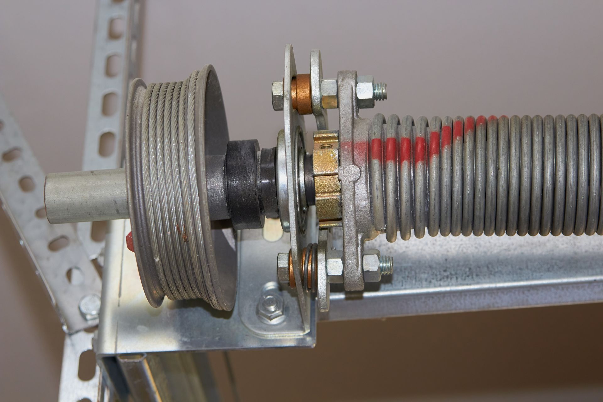 Close-up of a metal pulley and coiled cable assembly with a red-marked spring on a mounting bracket