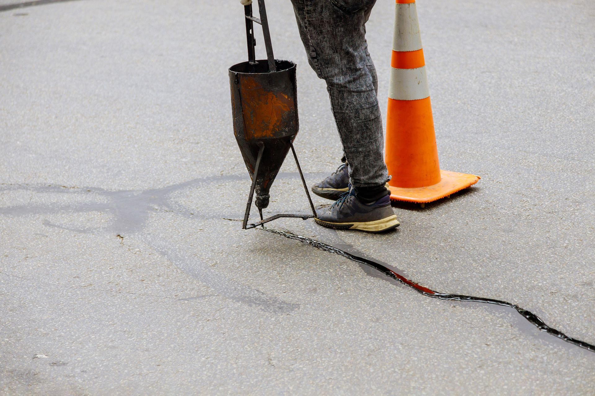 Technician applying hot rubber crack filler with pour pot and squeegee