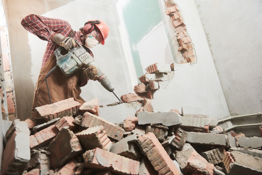 A Man Is Breaking Bricks With A Hammer In A Room — ACC Excavations & Demolition Pty Ltd In Oak Floats, NSW
