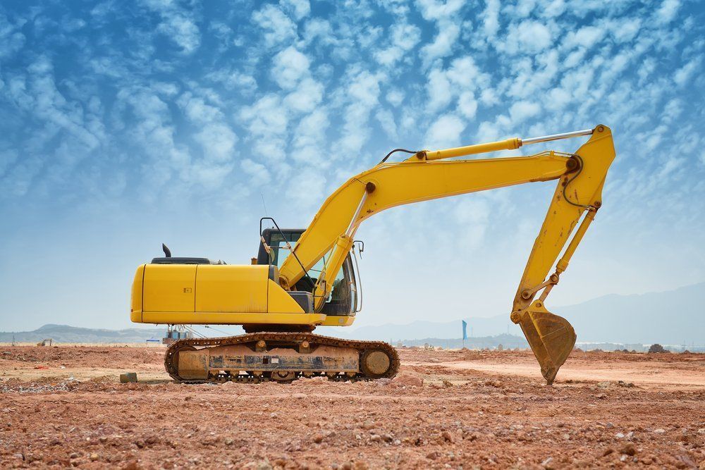 A Yellow Excavator Is Sitting In The Middle Of A Dirt Field — ACC Excavations & Demolition Pty Ltd In Shellharbour, NSW