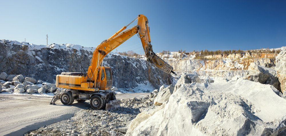 A Yellow Excavator Is Working On A Pile Of Rocks In A Quarry — ACC Excavations & Demolition Pty Ltd In Ulladulla, NSW