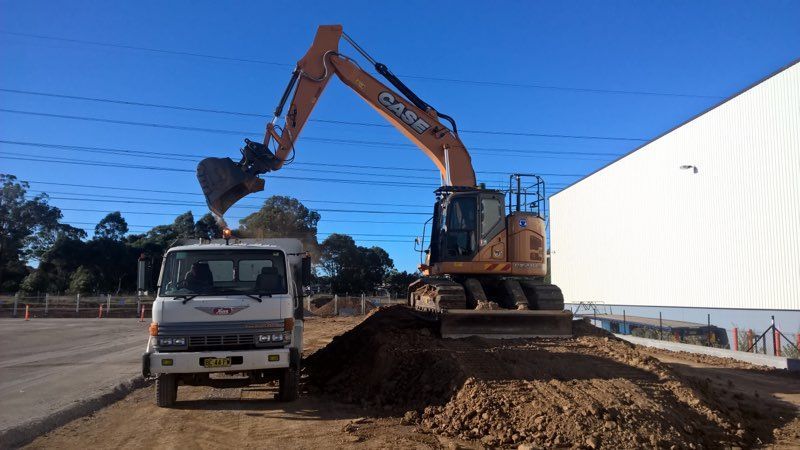 A Case Excavator Is Loading Dirt Into A Truck — ACC Excavations & Demolition Pty Ltd In Shellharbour, NSW