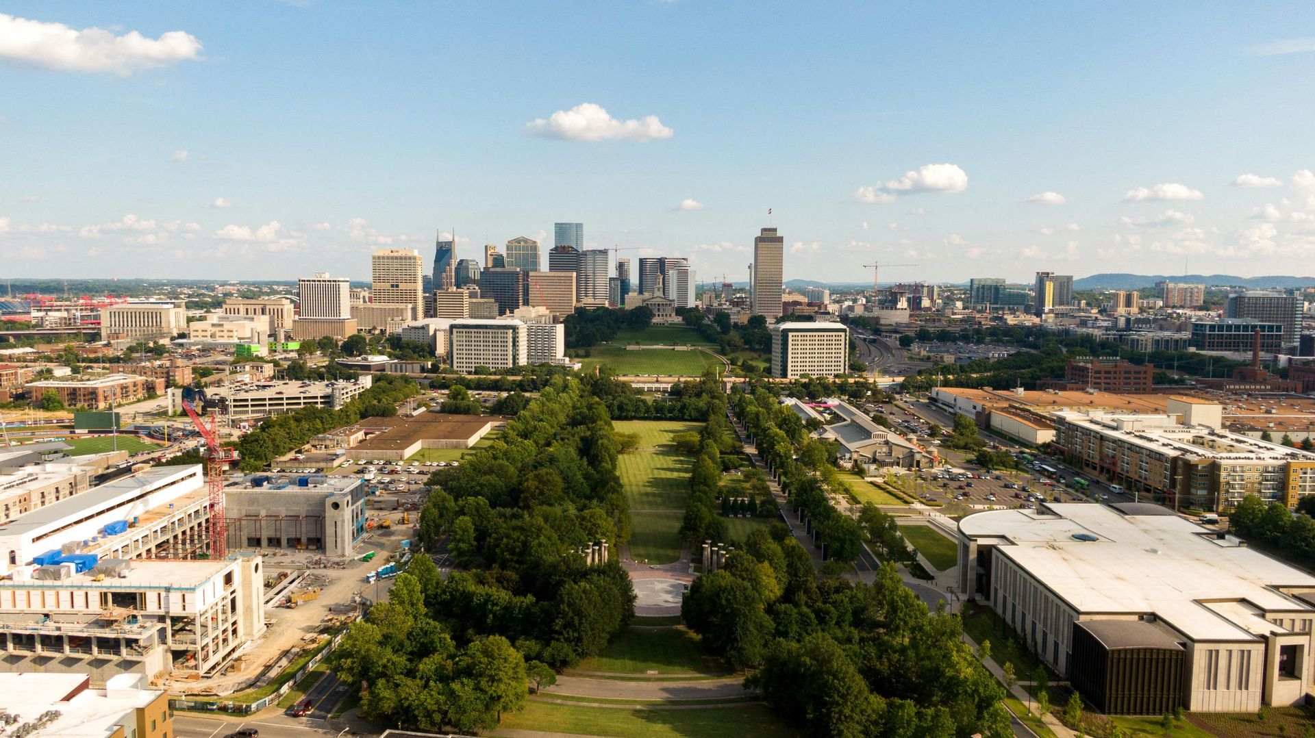 Downtown Nashville skyline seen over a greenway on a sunny day. Buildings and trees.