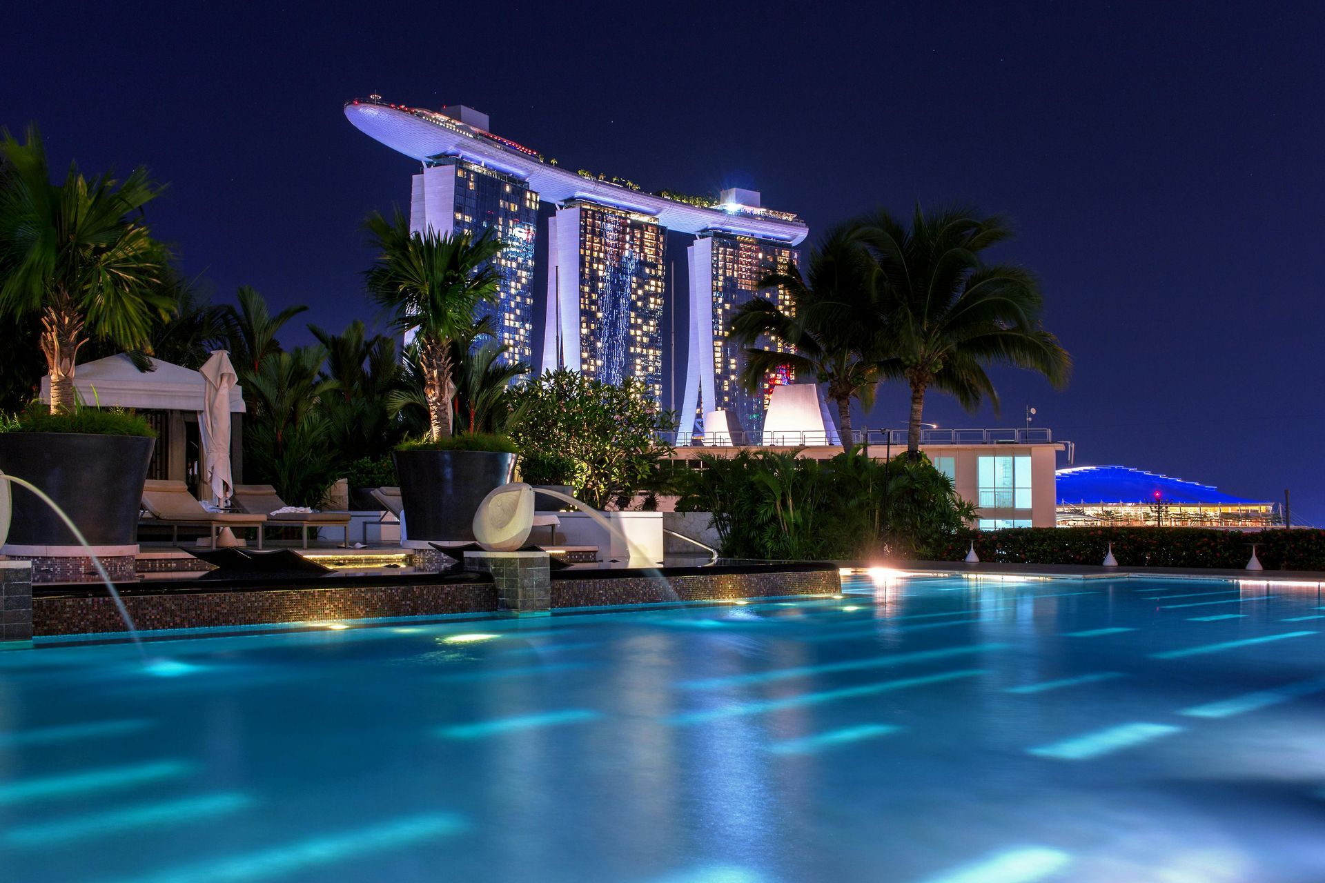Pool overlooking the illuminated Marina Bay Sands hotel in Singapore at night.