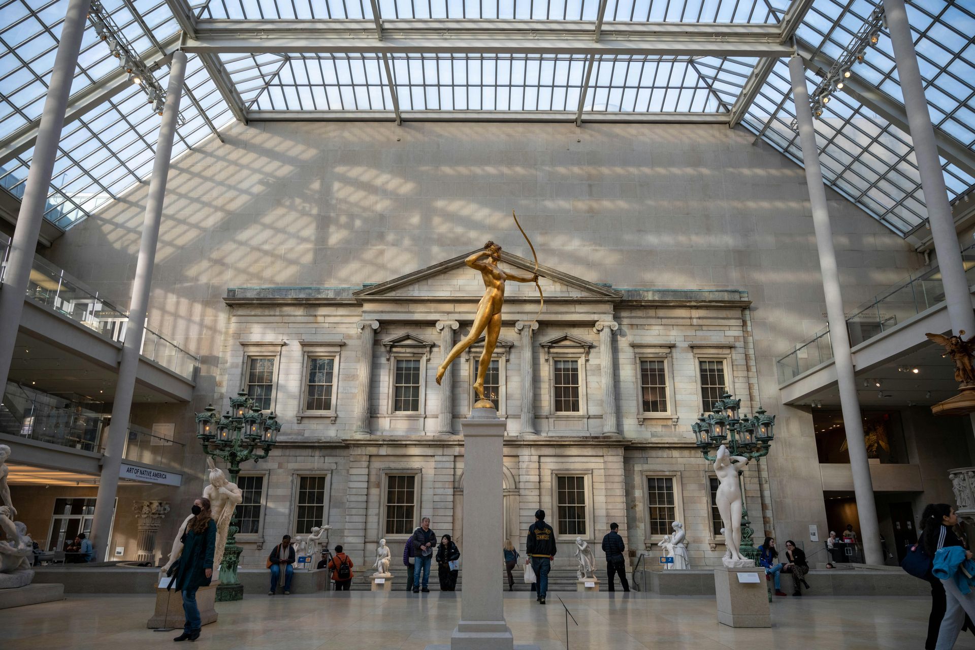 Interior of the Metropolitan Museum of Art with a large statue and people below, lit by a glass ceiling.